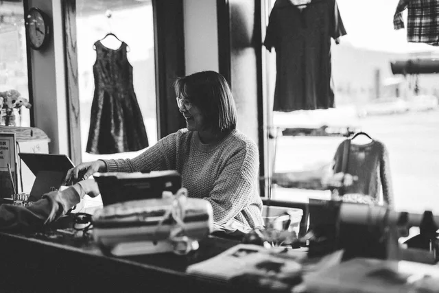 A woman happily assisting a customer at a thrift store counter in Minnesota, USA. Obsługa klienta w małej firmie: standardy, kanały i reklamacje